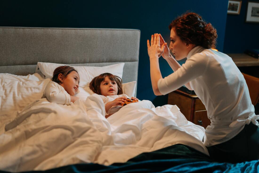 Woman in a white shirt telling a bedtime story to two kids in bed