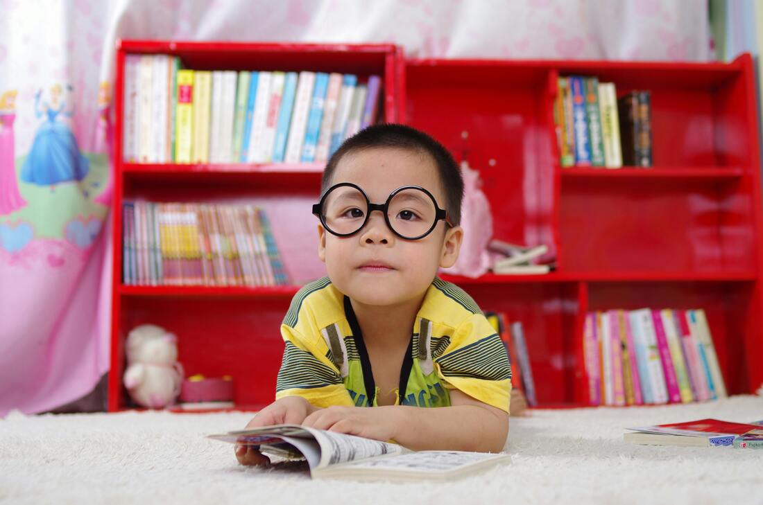 Little kid with glasses and a big red bookshelf behind him